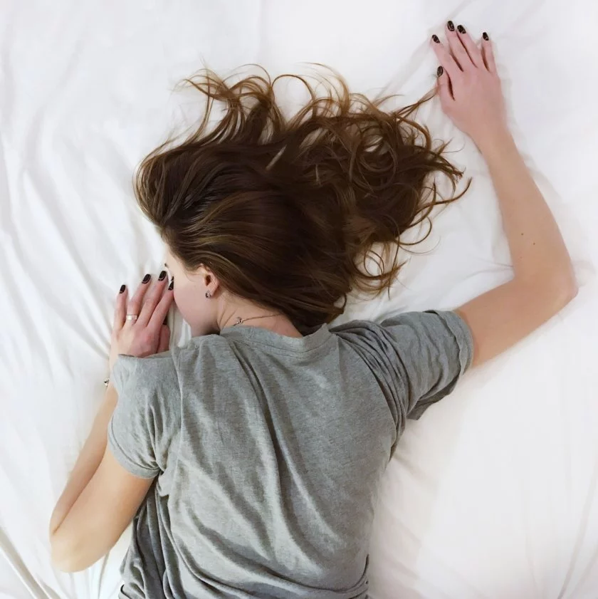 En kvinna ligger på mage i en säng och tittar ner i lakanet