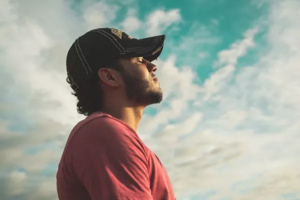 En man med en keps på huvudet tittar upp mot en blå himmel