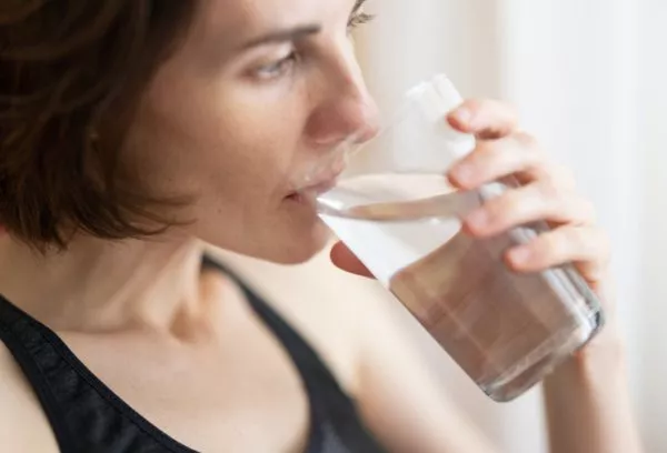 En närbild på en kvinna med kort mörkt hår som dricker ur ett stort glas med vatten.