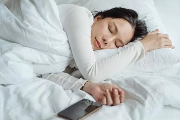 En kvinna sover på en säng med mobilen bredvid sig