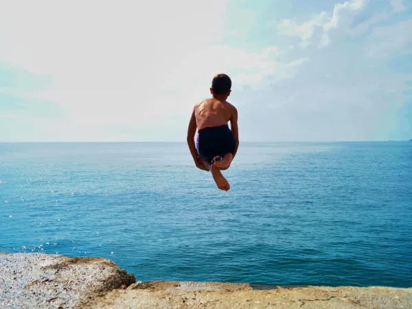 Pojke hoppar ner i vattnet från en klippa