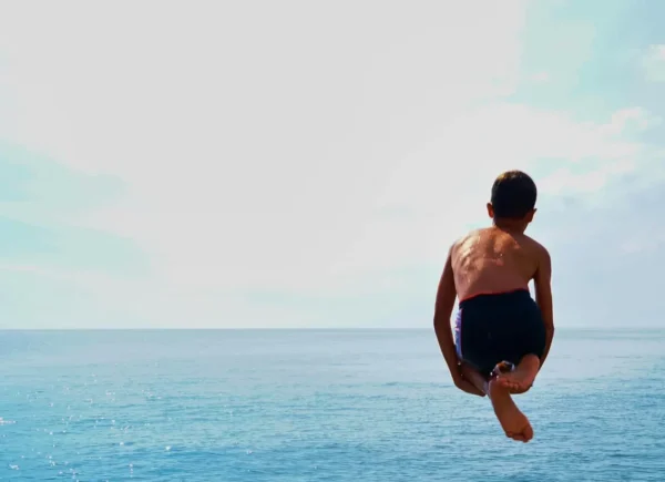 Pojke hoppar ner i vattnet från en klippa